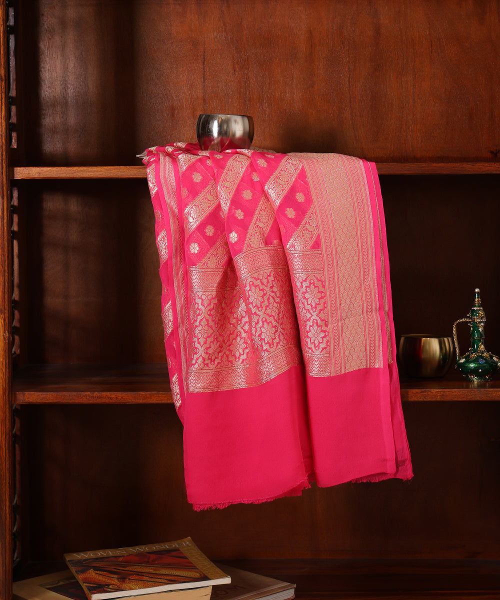 Coral pink handloom georgette dupatta draped over a wooden cabinet, showing its chevron-inspired zari weave, floral border and plain end section.
