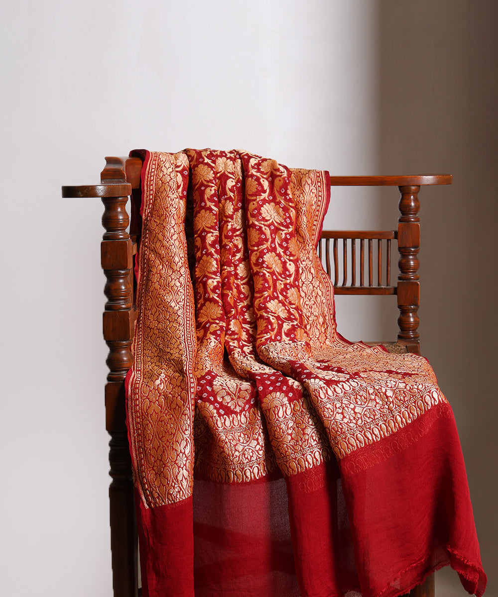 Maroon handloom Banarasi Bandhej dupatta draped over a wooden chair, featuring cutwork zari motifs, elaborate borders and a richly patterned palla.