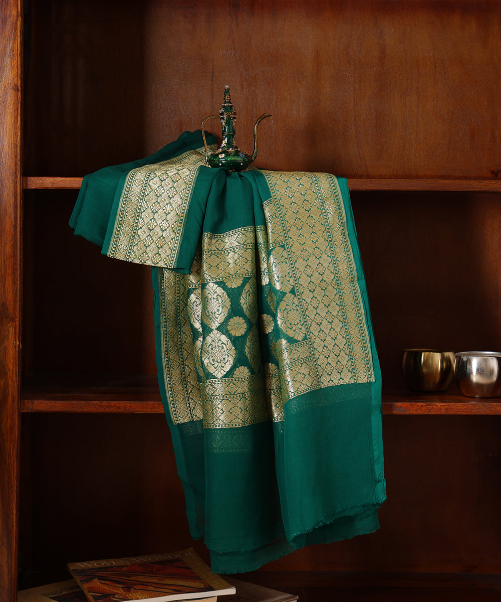 Green handloom Banarasi dupatta draped over a wooden cabinet, showing its floral gold zari palla and patterned borders.