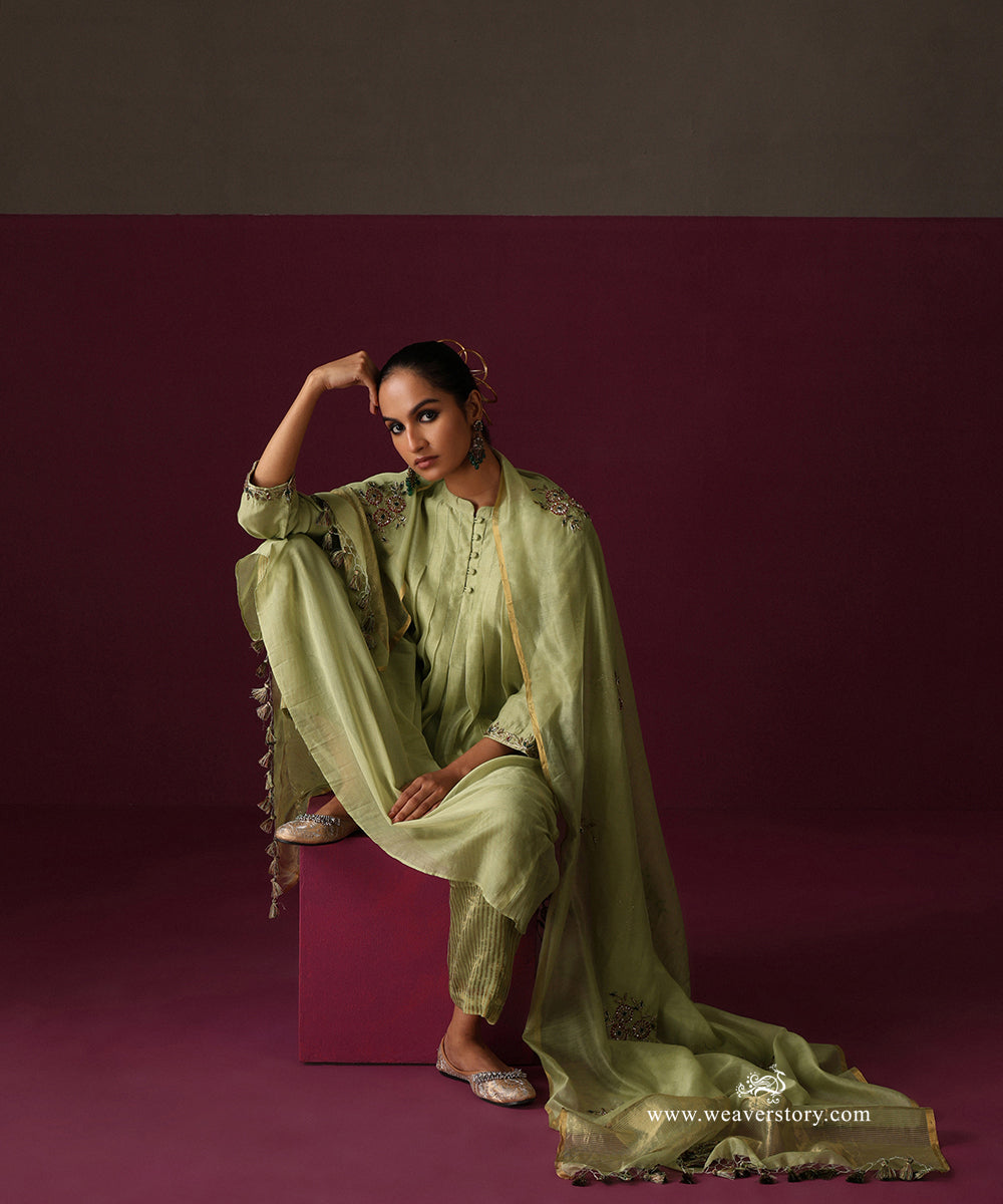 Seated view of the pista green Chanderi suit with floral embroidered dupatta and striped tissue pants