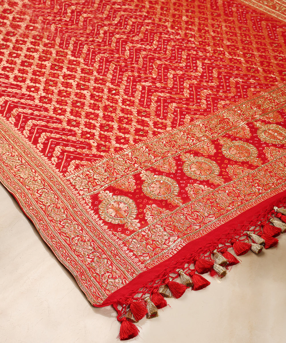Detailed view of red Bandhani dupatta featuring chevron Bandhej patterns, circular palla motifs and intricate floral borders.