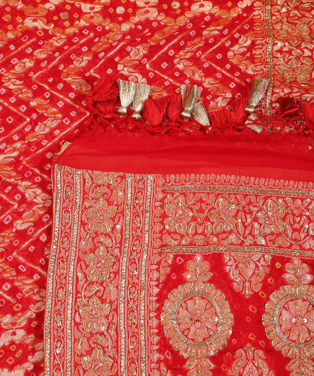Close-up of red Khaddi georgette Bandhani dupatta with floral zardozi highlights, ornate borders and red-and-gold tassels.