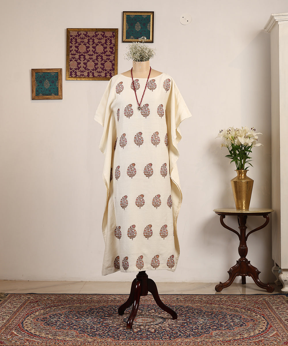 White dress with red floral patterns on a mannequin against a neutral wall with decorative elements.