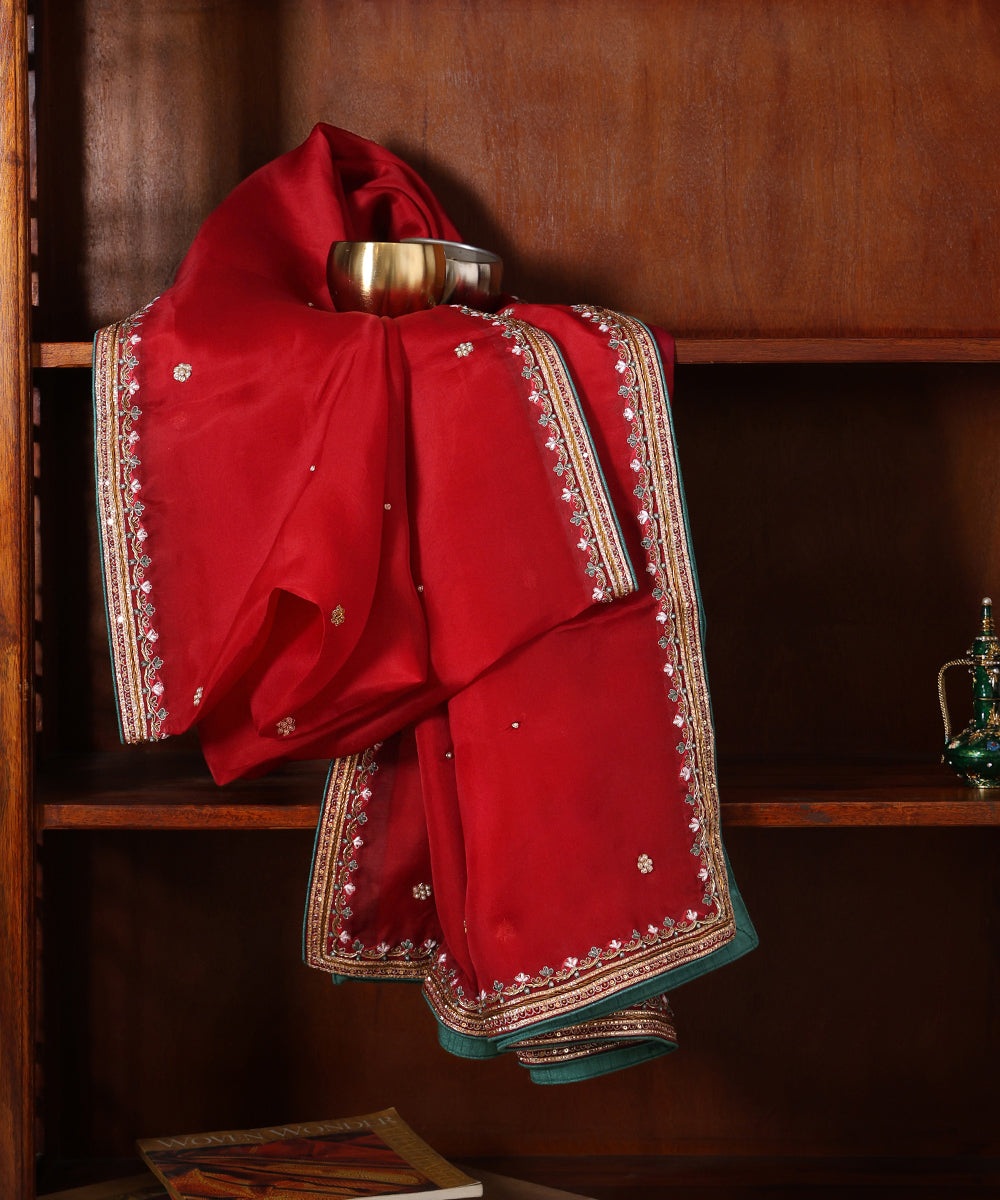 Red organza dupatta displayed against a wooden cabinet, featuring fine hand embroidery, delicate bootis and deep green finishing