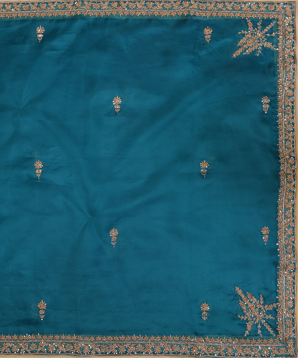 Full view of Firozi blue organza dupatta with zardozi bootis, a floral-vine border and elaborate motifs at the corners.