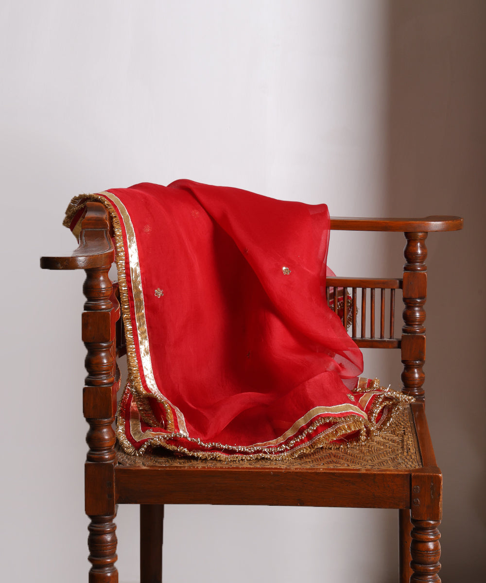 Red silk organza dupatta draped over a wooden chair, featuring scattered floral zardozi bootis and a lampi gota border with metallic kiran.
