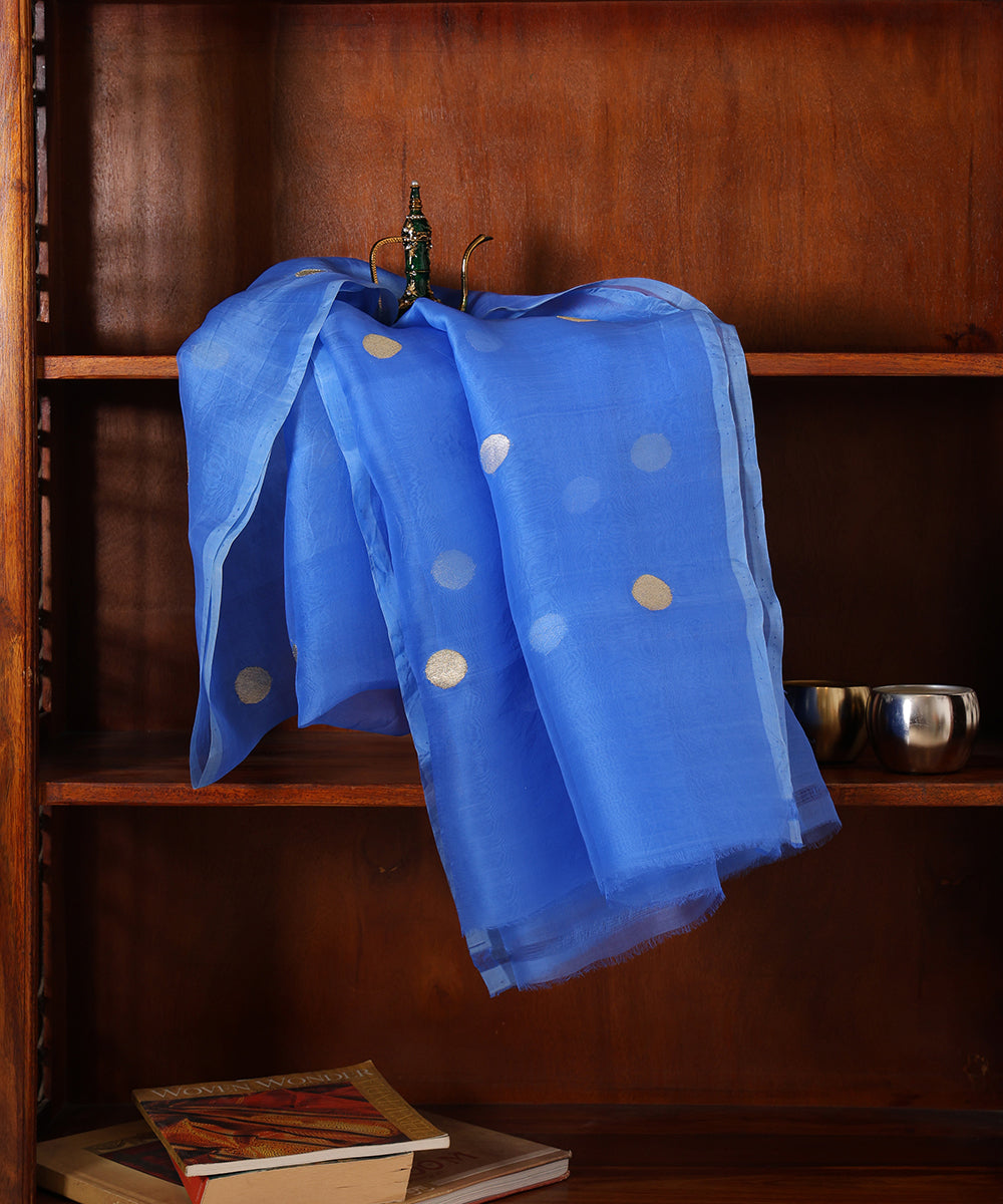 Royal blue handloom organza silk dupatta draped against a wooden cabinet, featuring gold and silver zari bootis and tonal edging.