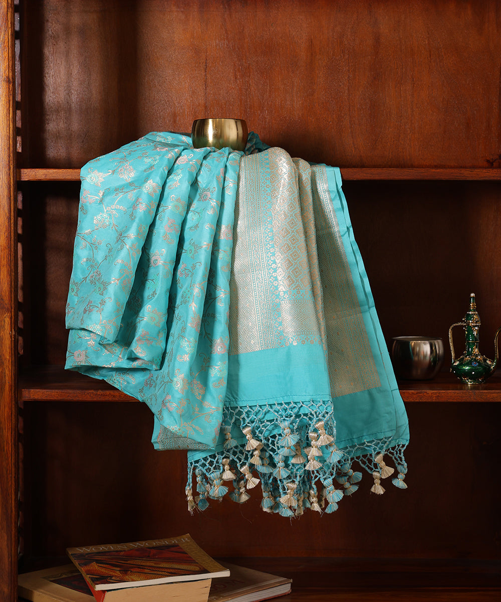 Light turquoise blue Banarasi Katan silk Jangla dupatta displayed against a wooden cabinet with a zari palla and handcrafted tassels.