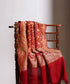 Maroon handloom Banarasi Bandhej dupatta draped over a wooden chair, featuring cutwork zari motifs, elaborate borders and a richly patterned palla.