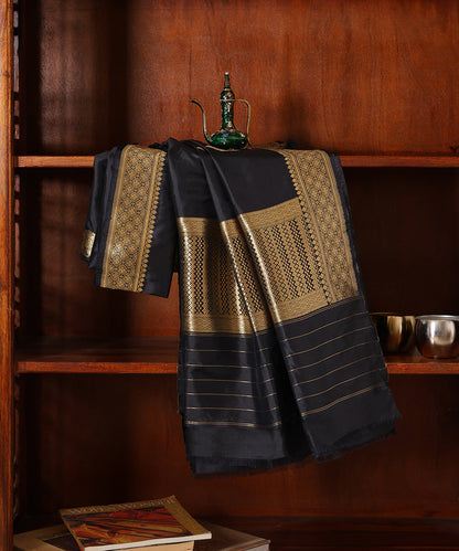 Black pure Katan silk Kadhwa dupatta displayed against a wooden cabinet, showing gold zari leaf bootis and geometric borders.