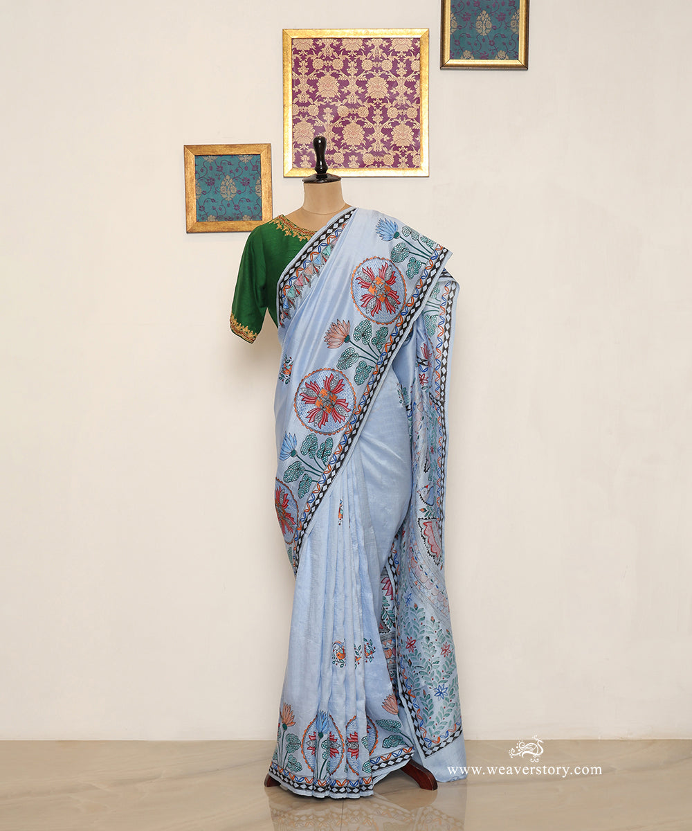 Full drape of sky blue Madhubani saree with painted fish circles, scattered birds and a black-and-white edge.