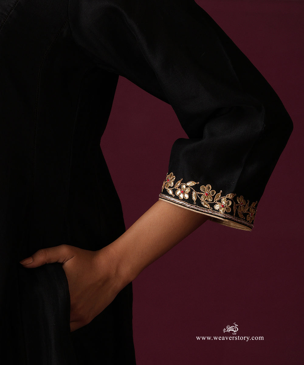Close-up of gold floral embroidery with small red accents along the black kurta cuff