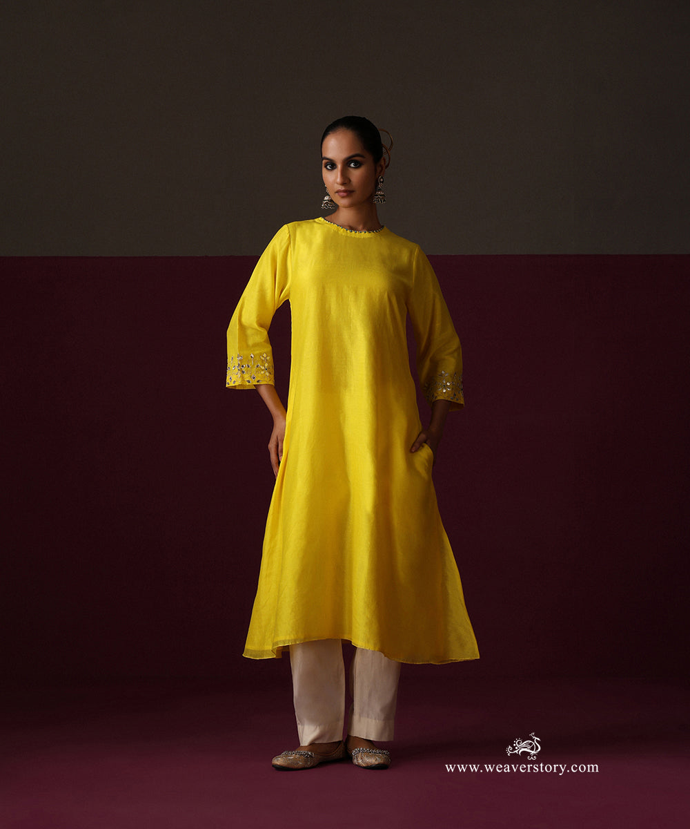 Front view of the gently flared yellow Chanderi kurta with embroidered sleeve cuffs and white pants