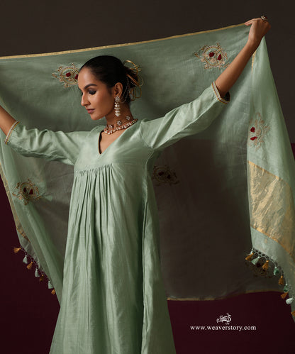 Model holding open the sage green dupatta to show its spaced embroidery, gold border and tassels