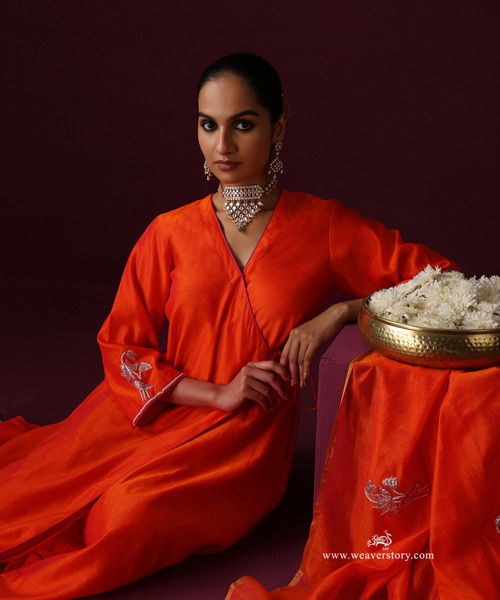Seated view of the orange Angrakha’s overlapping neckline, pink piping and embroidered sleeve cuff