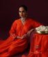 Seated view of the orange Angrakha’s overlapping neckline, pink piping and embroidered sleeve cuff