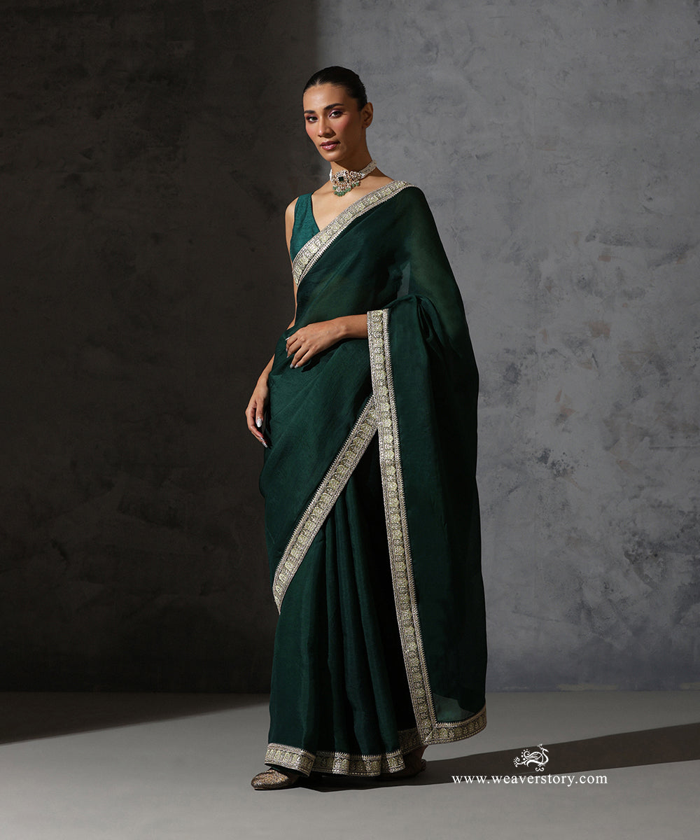 Full draped view of Nandini bottle green organza saree highlighting the plain body and handcrafted embroidered border.