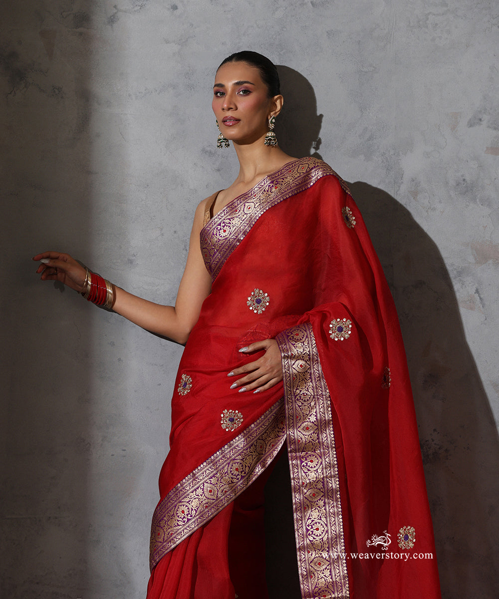 Front detail of Kaushiki red organza saree highlighting hand-embroidered zardozi meenakari bootis and the paisley and floral zari work of the purple Banarasi border
