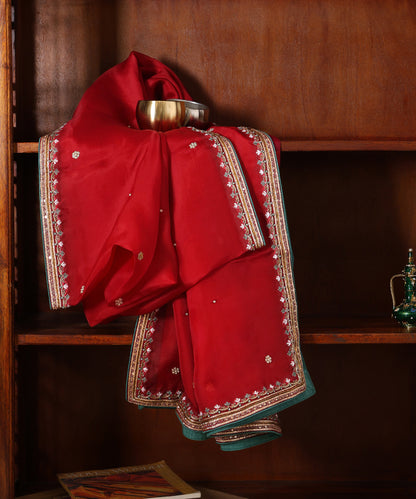 Red organza dupatta displayed against a wooden cabinet, featuring fine hand embroidery, delicate bootis and deep green finishing