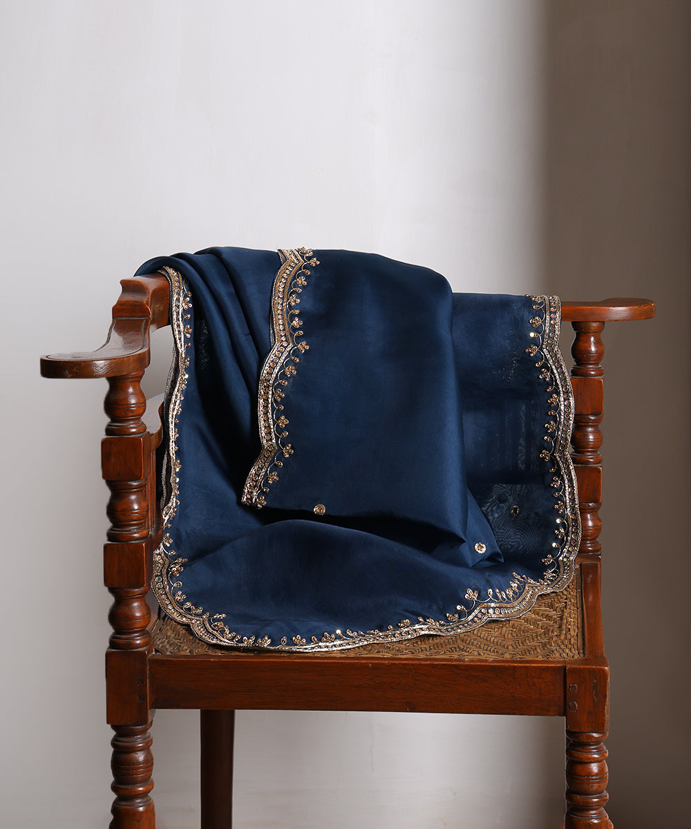 Teal blue silk organza dupatta draped over a wooden chair, featuring scattered zardozi bootis and a hand-embroidered metallic scalloped border.