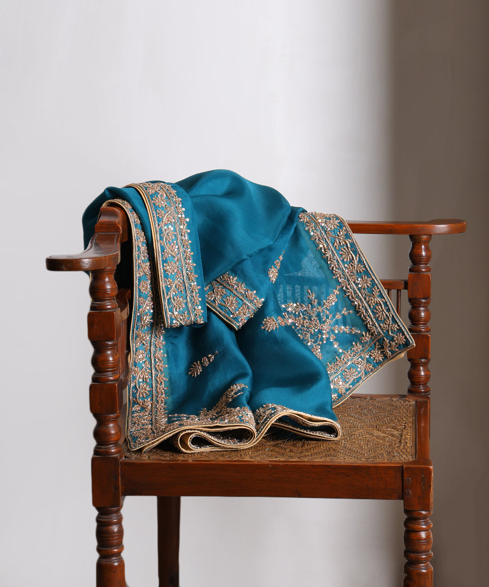 Firozi blue Luxury Edit organza dupatta draped over a wooden chair, showcasing intricate metallic zardozi embroidery and ornate floral borders.