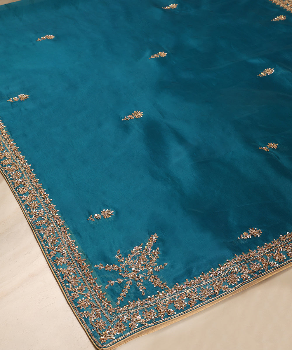 Angled view of Firozi blue organza dupatta featuring scattered bootis, an ornate zardozi border and statement floral corner embroidery.