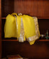 Yellow silk organza dupatta displayed against a wooden cabinet, showing its sheer body and luminous gold lampi gota border
