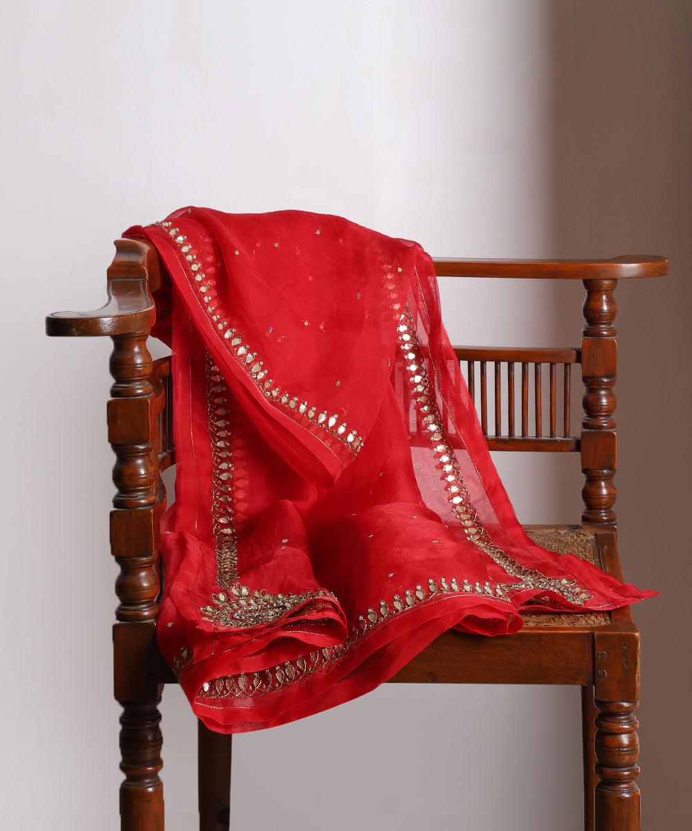 Close-up of red silk organza dupatta with scattered sequins, a hand-embroidered gota patti border and an ornate circular corner motif.