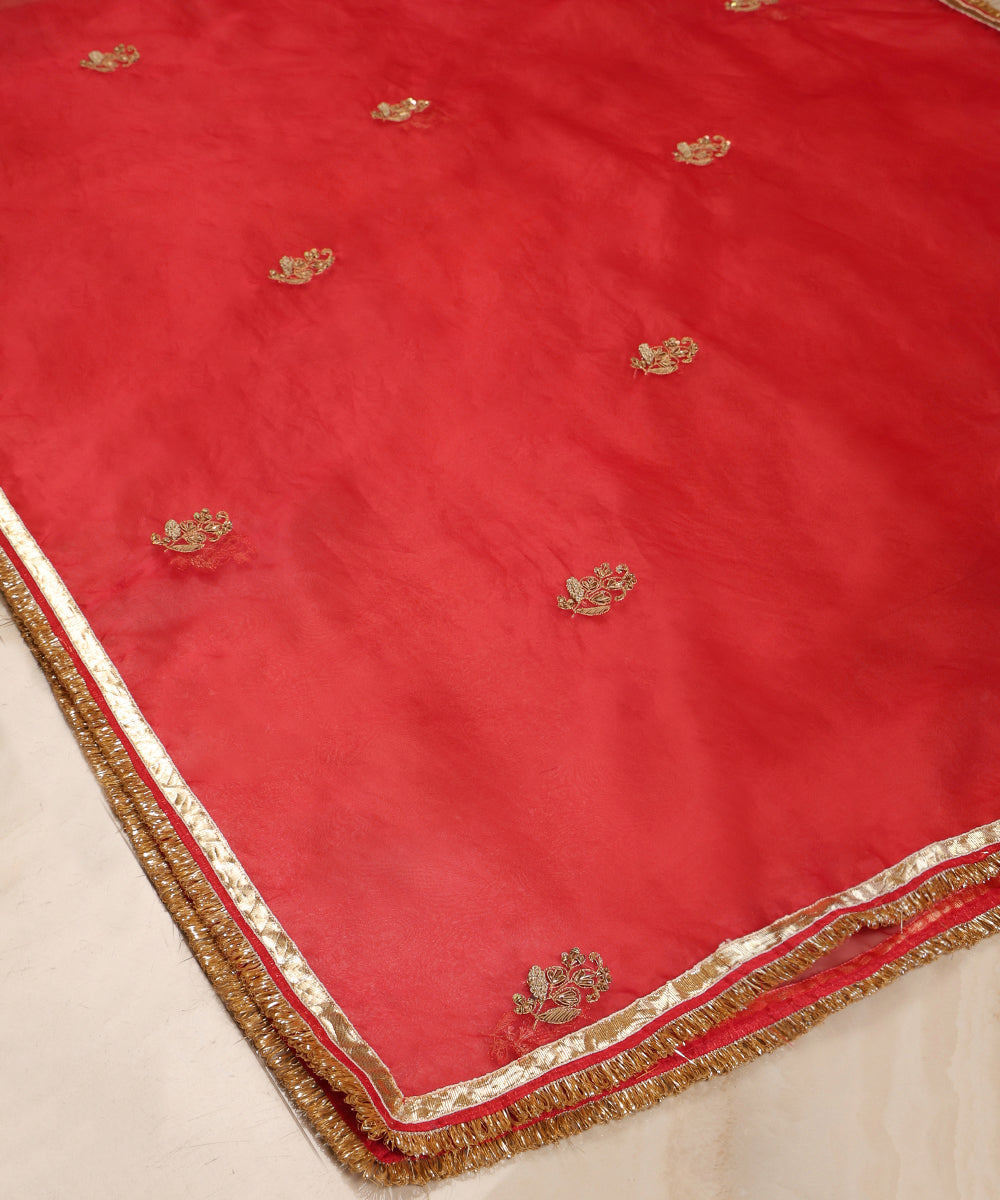 Red organza dupatta draped over a wooden chair, showing its sheer texture, metallic farisha bootas and handcrafted gota-kiran border.