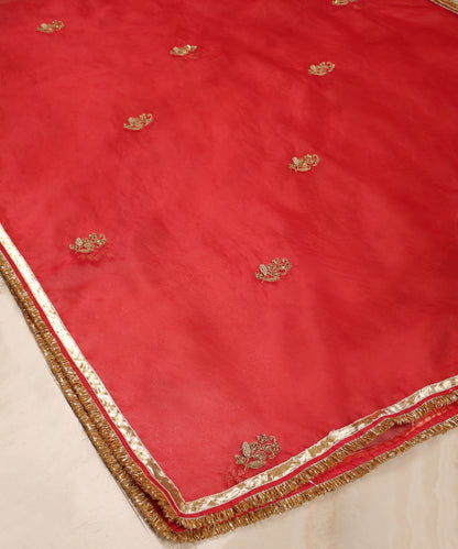 Red organza dupatta draped over a wooden chair, showing its sheer texture, metallic farisha bootas and handcrafted gota-kiran border.
