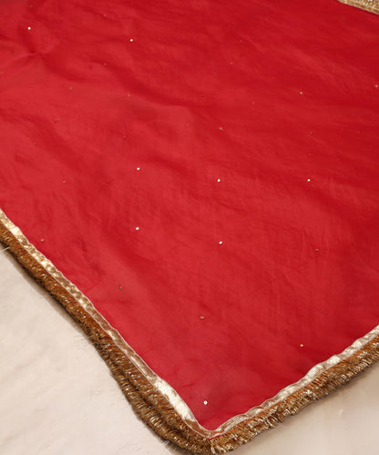 Red silk organza dupatta draped over a wooden chair, showing its sheer texture, scattered sequins and metallic kiran-finished border.